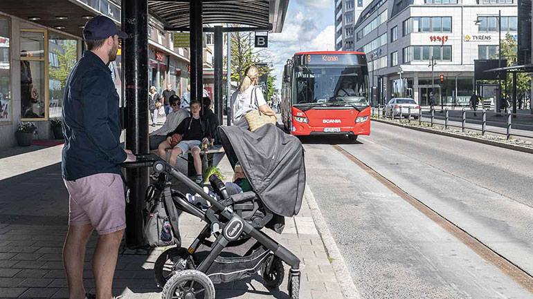 Pappa med barnvagn väntar på buss på Smedjegatan.
