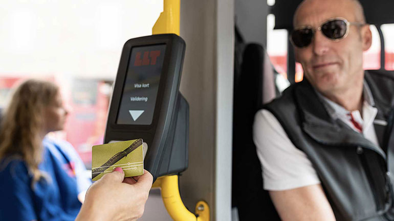 Närbild på hand som håller busskort mot betalningsautomat på buss.