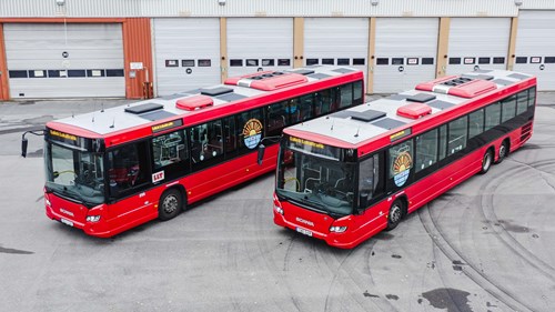 Två LLT bussar, solcellshybrider står parkerade framför bussgaraget